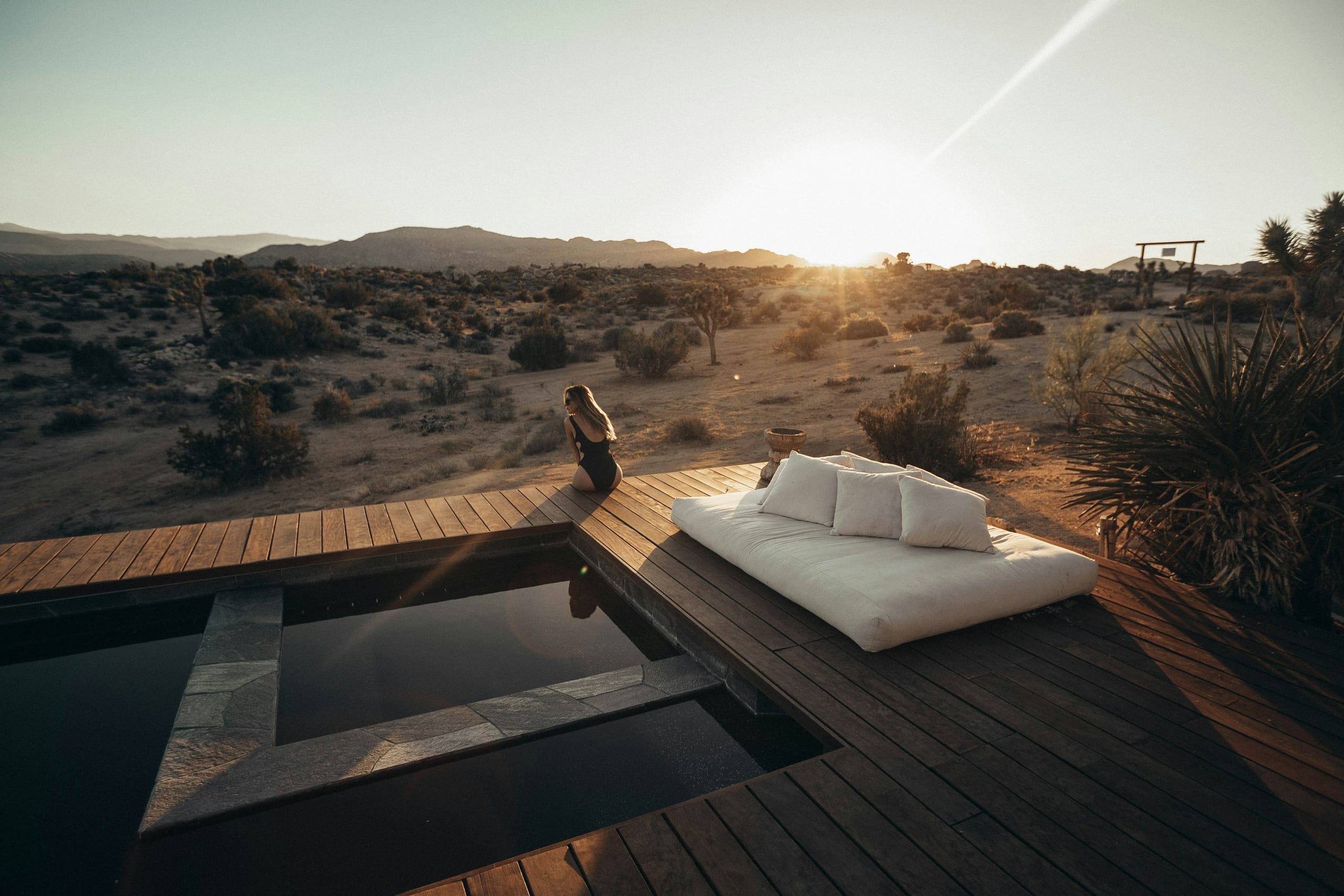 A daybed on a wooden deck beside a plunge pool at sunset